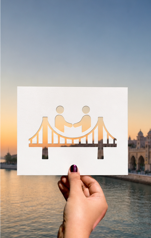 A paper cutout of a handshake over a bridge framing a sunset waterfront